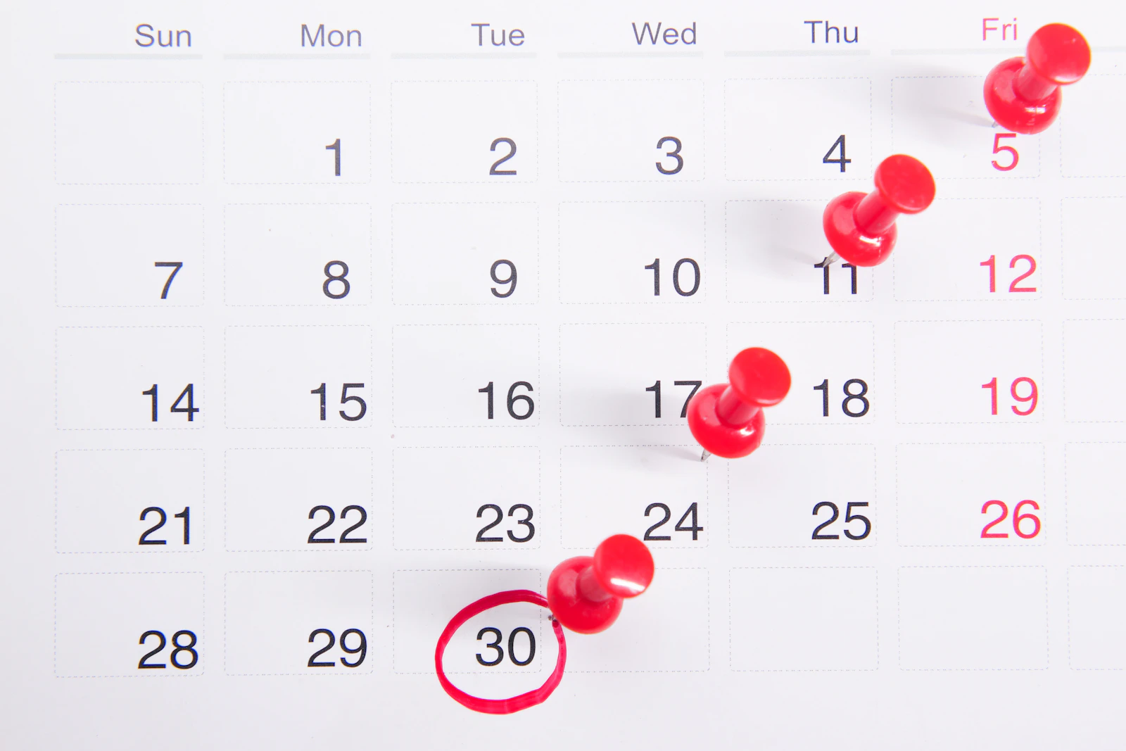 A wall calendar with red push pins marking dates through the month