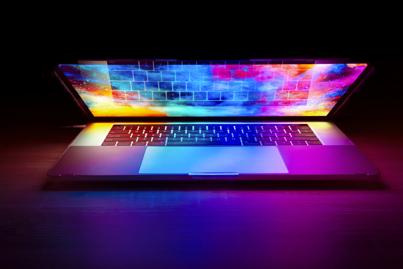 A laptop with a glowing, colourful screen on a dark desk